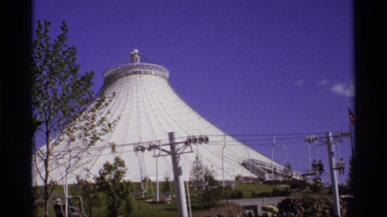 White tent-like dome with cable-car supports, trees, and a purple-blue sky.