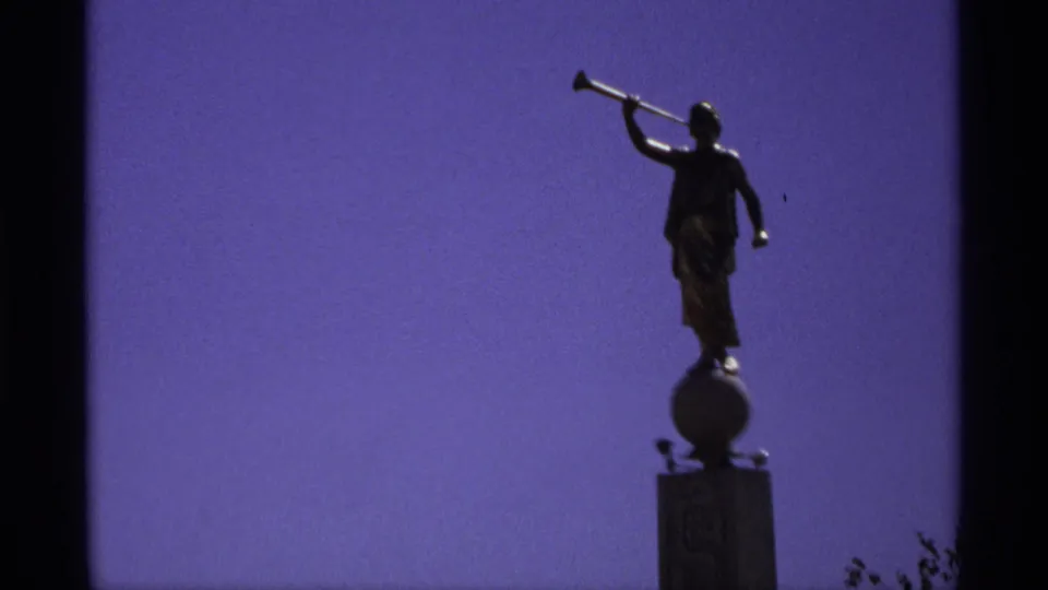 A dark statue figure holds a horn to its mouth, seen in silhouette with sparse foreground foliage at the frame edge.