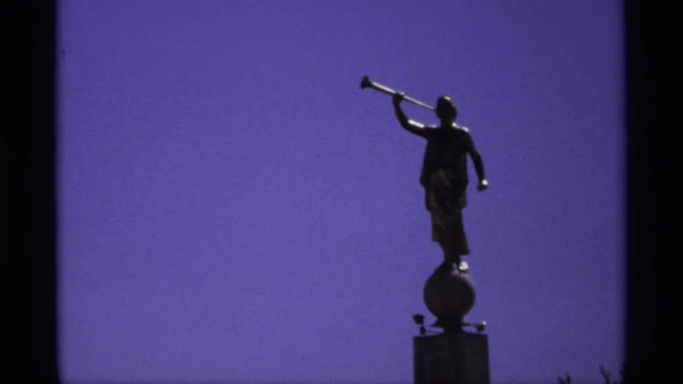 Low-angle 8mm view of the silhouetted horn statue on its round base, with the pedestal partly visible below.