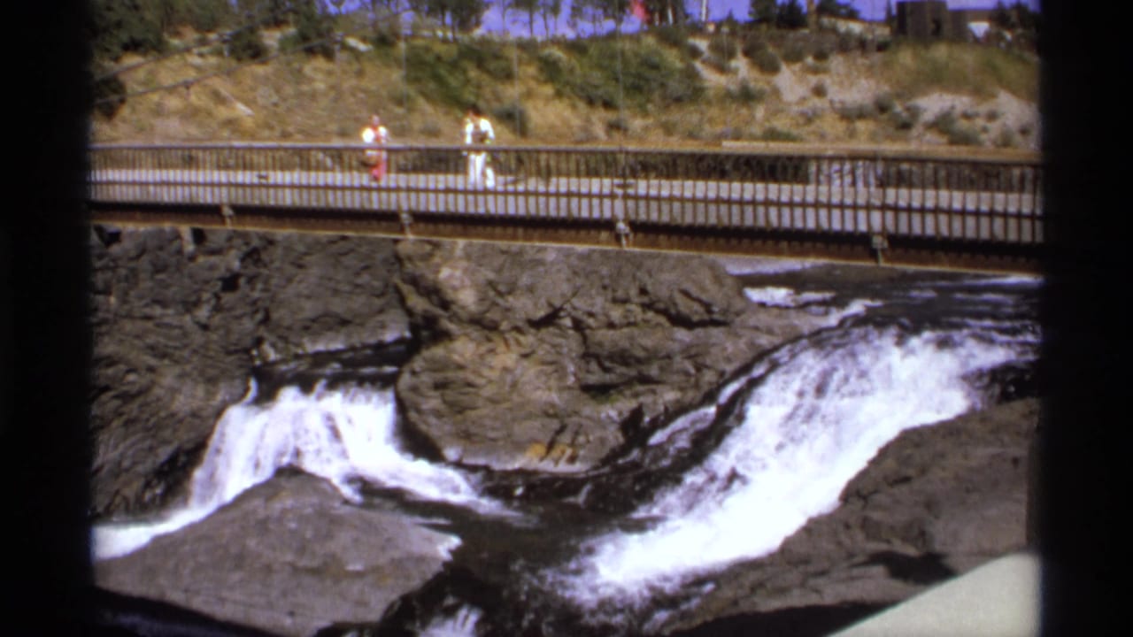 Waterfall running through rocks below a pedestrian bridge with visitors above.