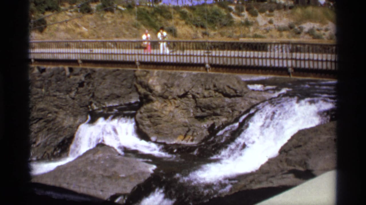 Visitors on a pedestrian bridge above a rocky waterfall and fast water.