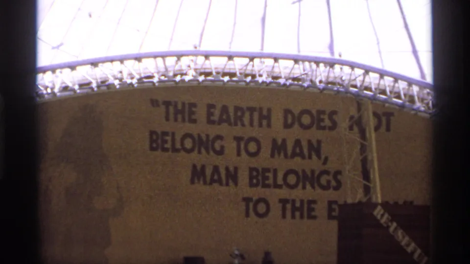 Tight 1970s 8mm frame of the dome wall with the quote, structural lattice above, and partial objects at the lower edge.