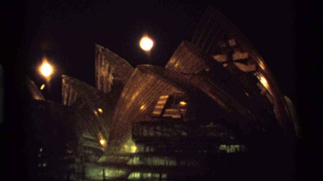 Night view of an illuminated sail-like modern building with bright lamps and dark sky.