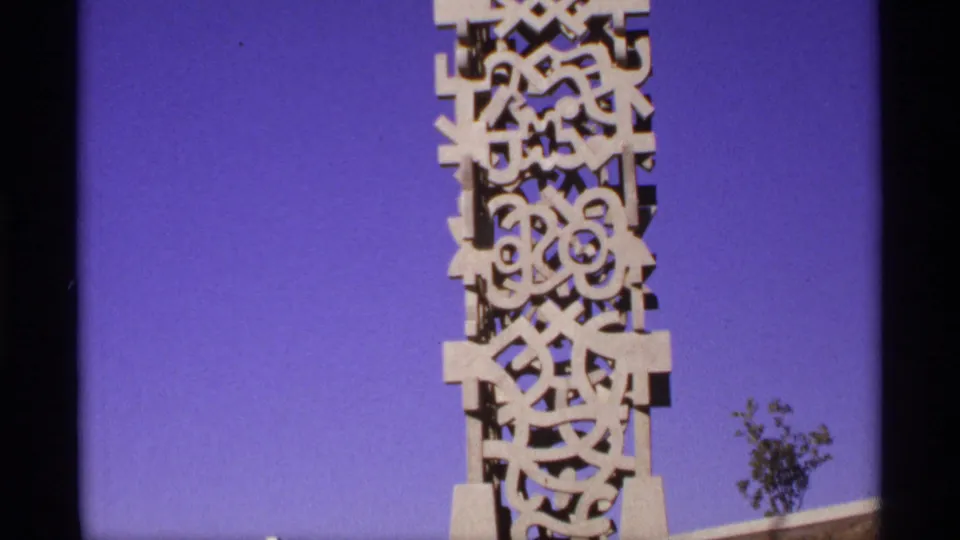 Close view of a tall carved white monument with geometric cutout forms against a saturated blue sky.