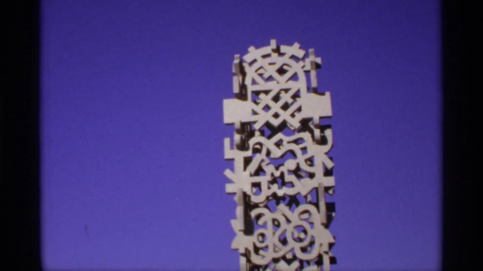 Close fairground shot of the upper section of a carved white monument with abstract geometric openings against blue sky.
