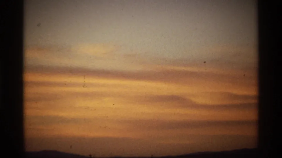 Golden-orange cloud layers drift over a dark ridge line in a scanned 8mm home-movie frame.
