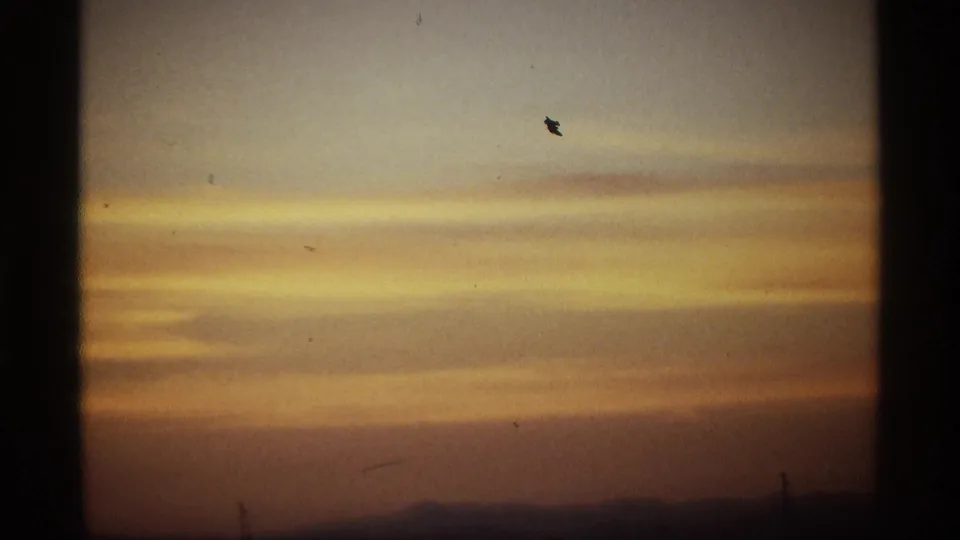Golden-yellow cloud layers stretch across the sunrise sky, with low hill silhouettes, small pole shapes, dust marks, and visible 8mm frame borders.