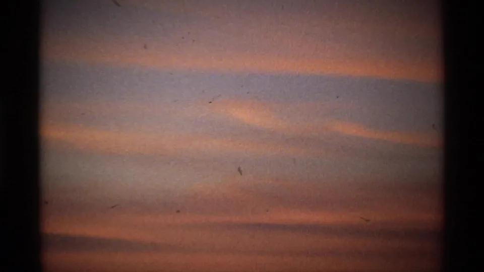 Soft pink and orange cloud layers at dawn, with a shadowed horizon, visible grain, dust specks, and dark vertical frame edges.