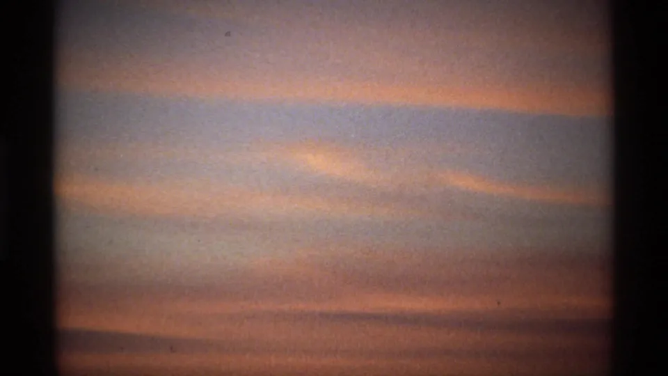 A softly exposed 8mm frame shows orange and pink clouds crossing a dim early-morning sky.