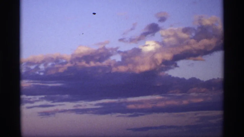 Pastel cloud formations stretch across the frame, with soft purple shadows, peach light, and visible 8mm film borders.