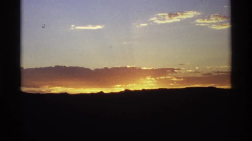 Blue sky and warm sunset clouds over a dark horizon, with the window frame dividing the 8mm view.