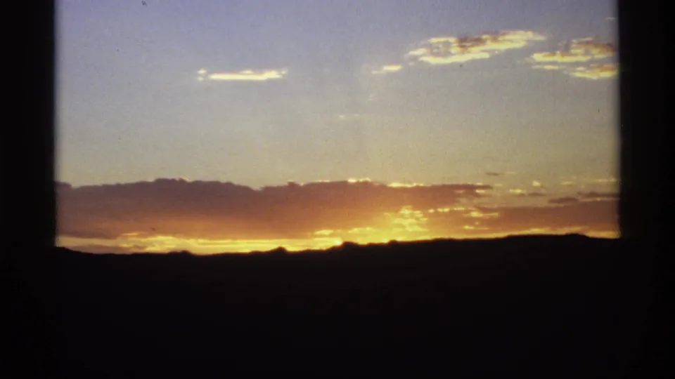 A home-movie sunset frame shows glowing yellow-orange light under clouds, with silhouetted hills below.