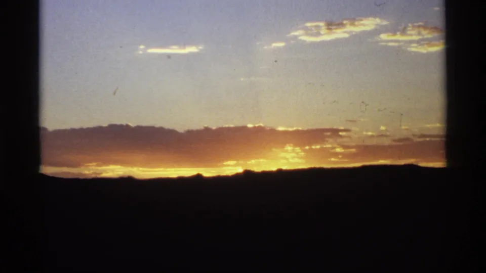 Final 8mm frame of a red-gold sunset over silhouetted hills, with small birds crossing the sky.