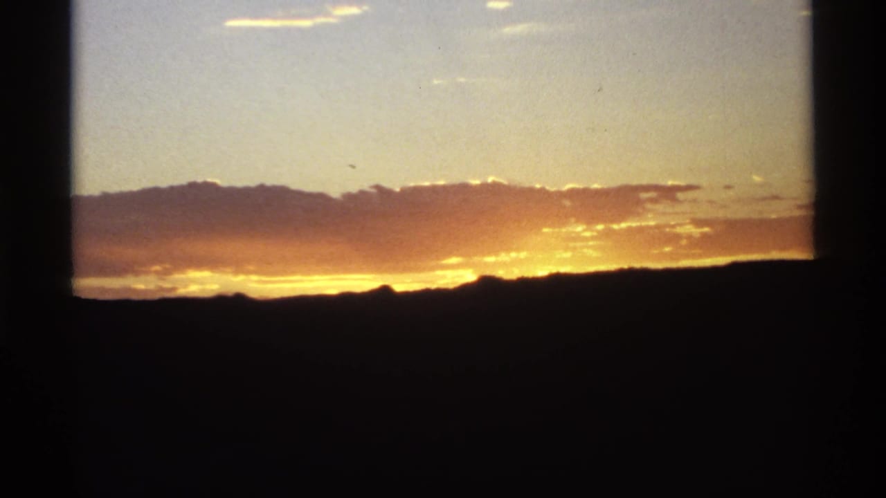 Golden sunset behind a dark mountain ridge with clouds and black frame edges.