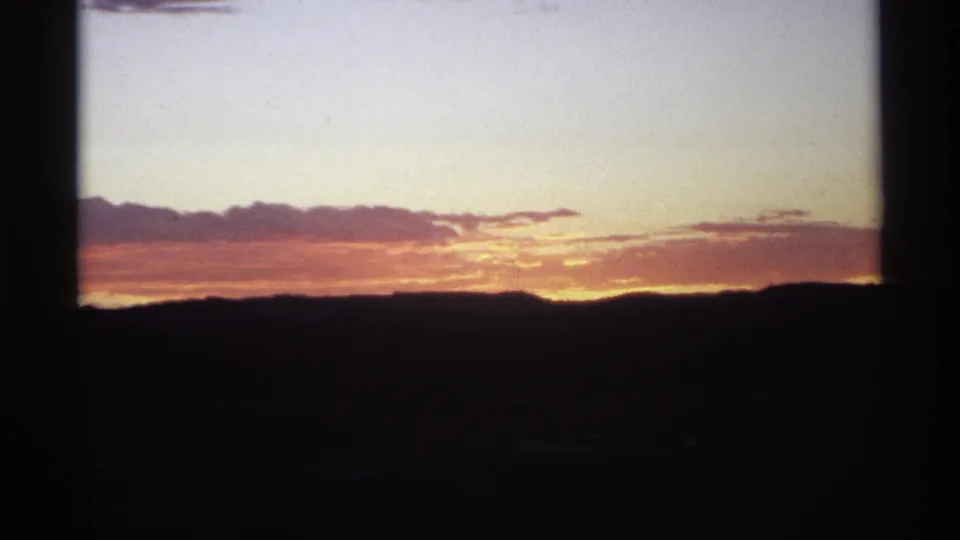 The sunset dims toward pink and amber tones over a silhouetted ridge, with soft grain and dark 8mm frame edges.