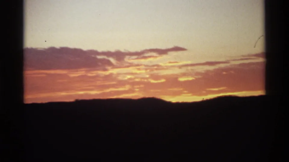 Warm sunset light and pink-orange clouds sit above a silhouetted ridge, framed by dark 8mm film borders.
