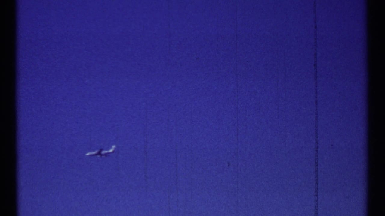 Small airplane crossing a cloudless blue sky in 1967 Montreal home-movie footage.