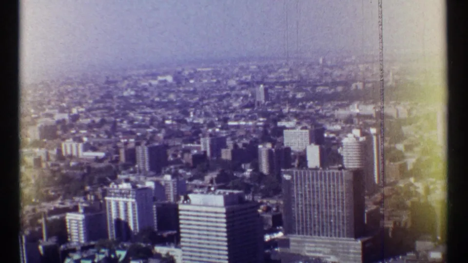 Wide 1967 Montreal aerial view with downtown towers, distant haze, and visible home-movie film wear.