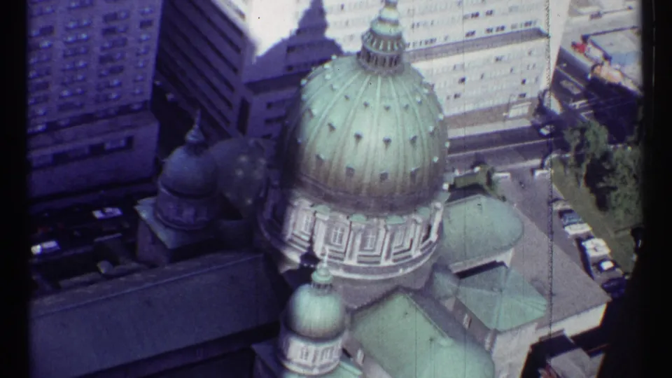 Clearer 1967 Montreal frame showing a large green church dome, smaller domes, rooftops, parked cars, and surrounding high-rises.