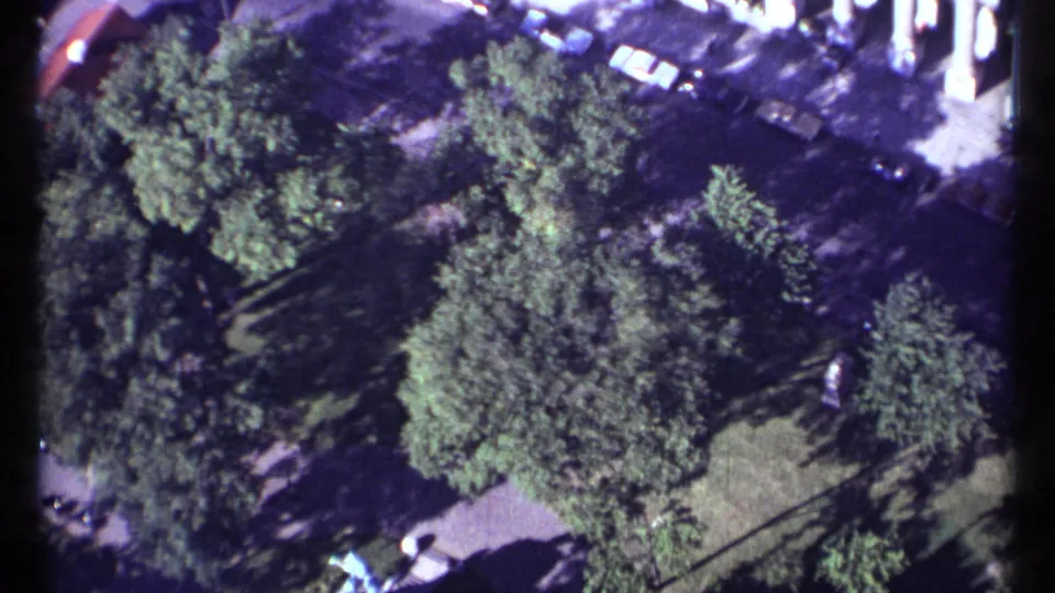 Late-clip 1967 Montreal aerial frame with a tree-filled park, visible lawn, paths, cars at the edge, and strong 8mm color flare.
