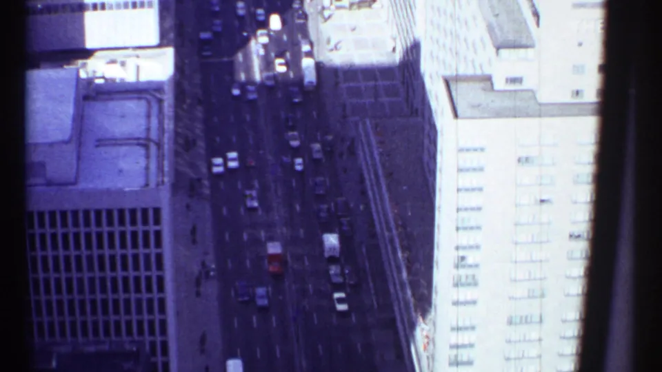 1967 Montreal aerial frame showing cars moving along a downtown street between high-rise buildings and sidewalks.