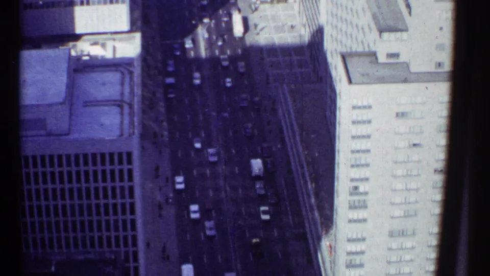 1967 Montreal 8mm frame showing a high-angle street view between tall downtown buildings with vehicles visible below.