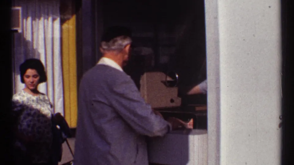 1967 Montreal amusement-park ticket booth scene with a suited man at the window and a woman standing behind him.