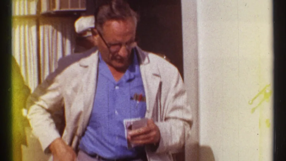 A man in glasses and a light jacket holds a ticket or small paper at the Expo 67 ticket area in Montreal.