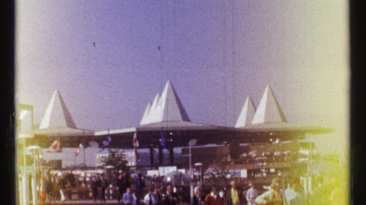 Crowds gather near white pointed roof structures at an outdoor fairground.