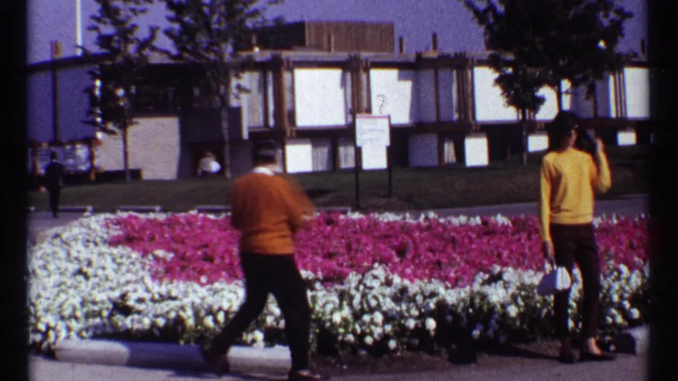 A man crosses in front of pink and white flowers as a woman stands nearby at the 1967 Montreal Expo fairgrounds.