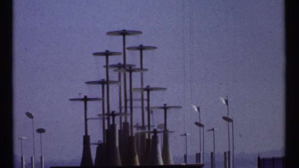 1967 Montreal frame with a cluster of modernist capped towers, streetlamps, and dark gate edge visible at left.