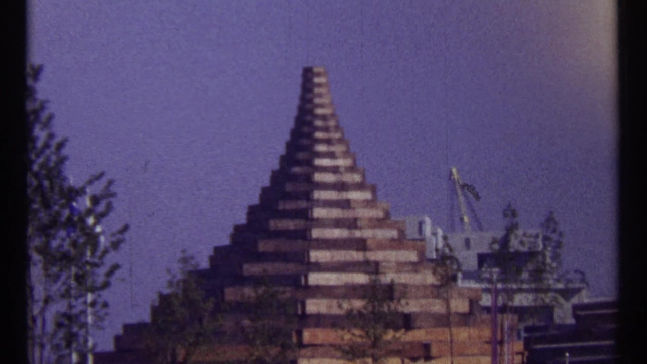 Stepped pyramid-like structure against blue sky with trees and construction equipment nearby.