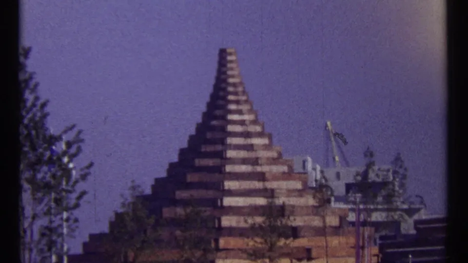 1967 Montreal 8mm frame showing a stepped geometric structure with trees in the foreground and equipment visible to the side.