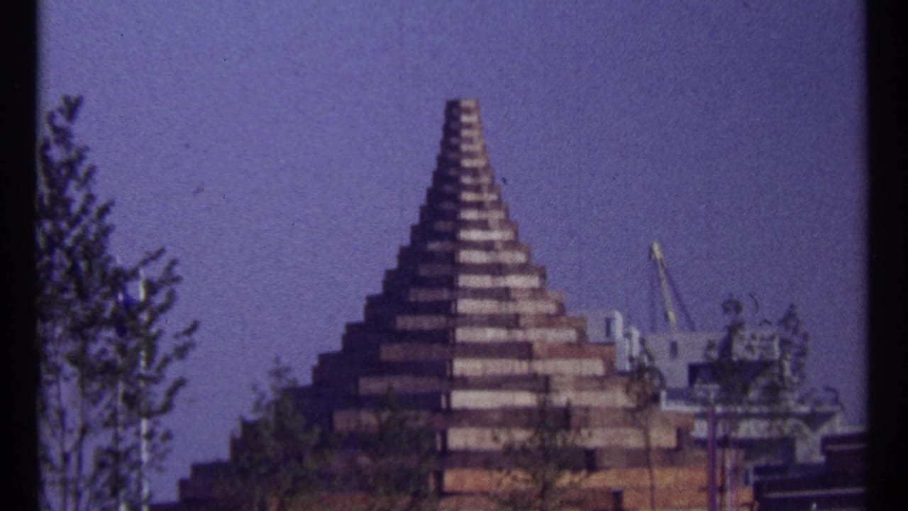 Stepped geometric structure framed by trees, with equipment visible at right.