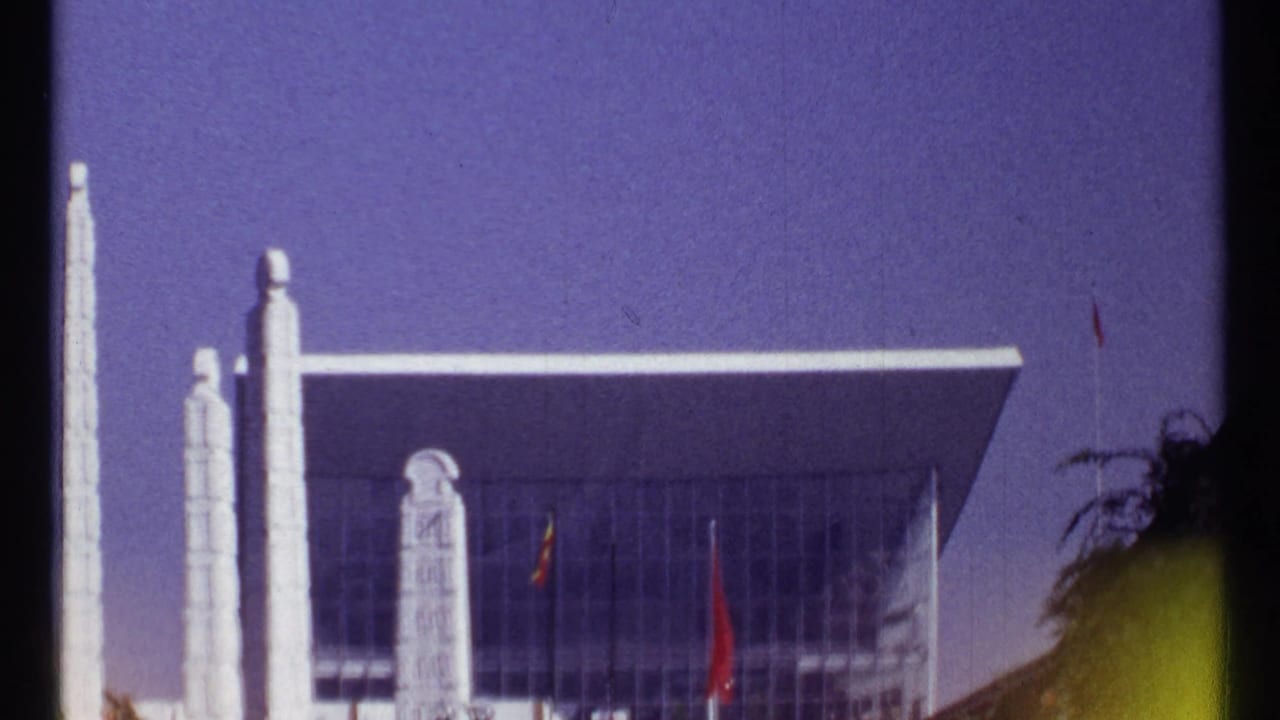 Glass modernist building with tall white pillars beneath a purple-blue sky.