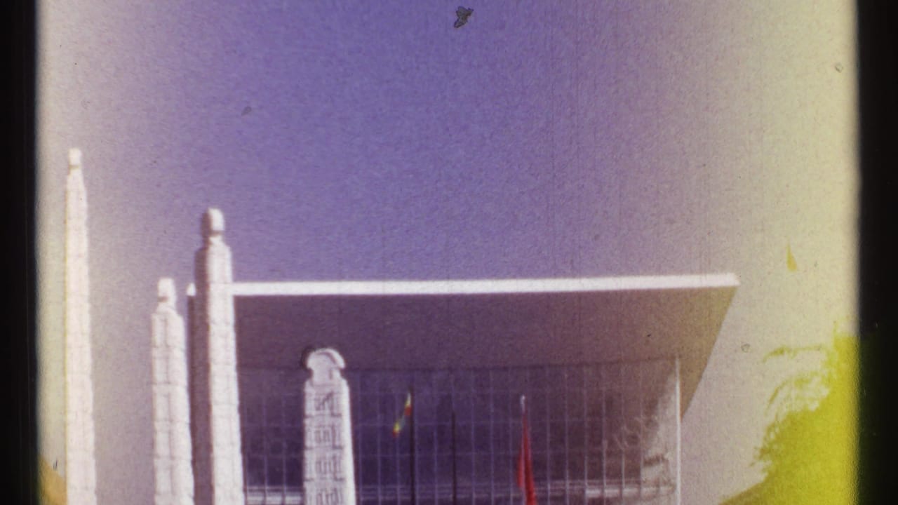 1967 Montreal home-movie frame with white pylons, a broad glass facade, flags, and visible color fading at the edge.