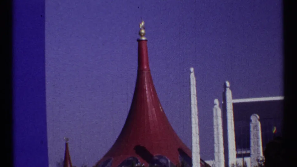 1967 Montreal frame showing a red conical roof with a gold finial near white pylons and the edge of a modern glass building.