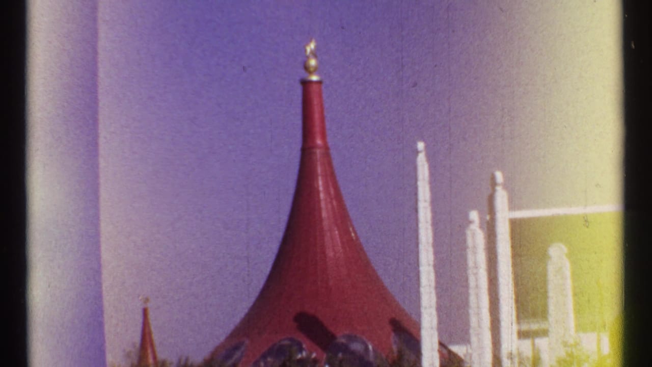 Red conical roof with gold finial beside white pillars under a purple-blue sky.