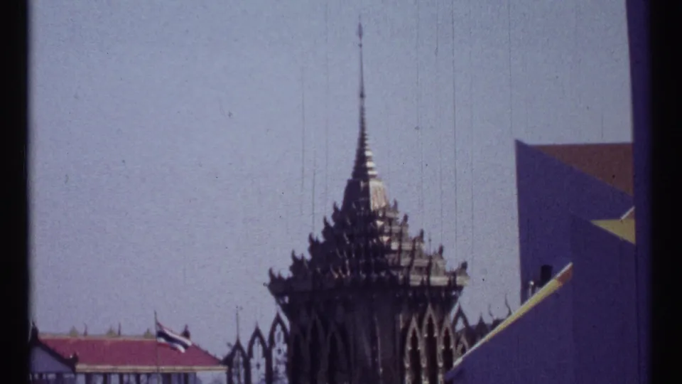 1967 Montreal 8mm frame showing a dark, ornate, tiered spire with flags and a sharply angled pavilion wall beneath a bright sky.