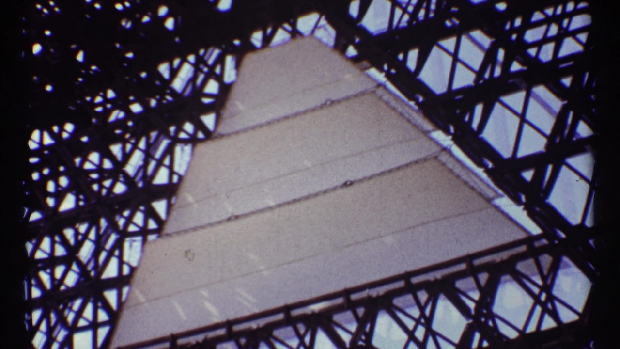 Low-angle 8mm frame of a Montreal monument structure with pale panels behind dark metal bracing.