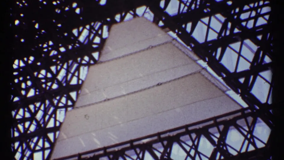 Low-angle 8mm frame of a Montreal monument structure with pale panels behind dark metal bracing.