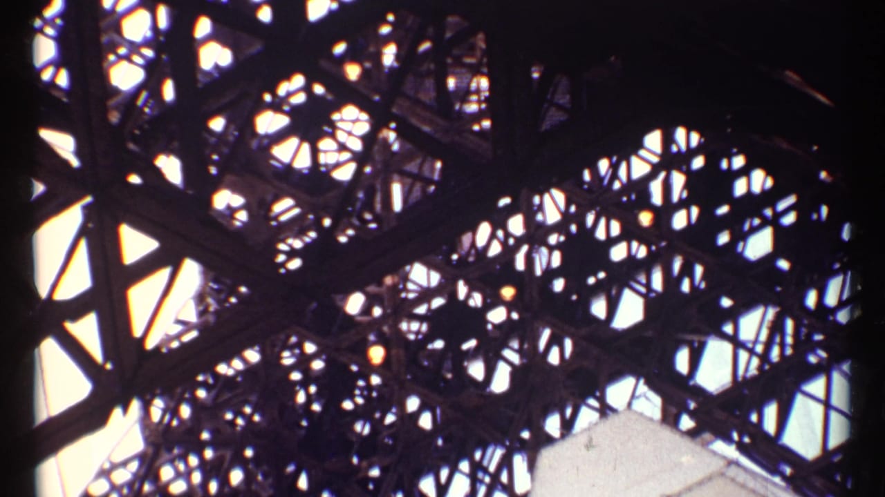 Low-angle view through dark steel latticework against a bright sky.