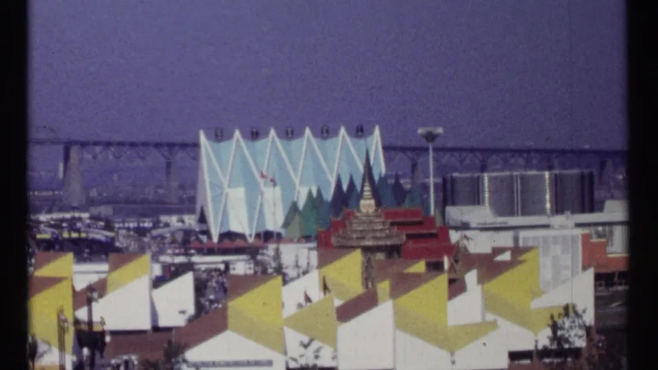 1967 Montreal Expo 67 view across yellow and white triangular pavilion roofs toward flags and a blue angular facade.