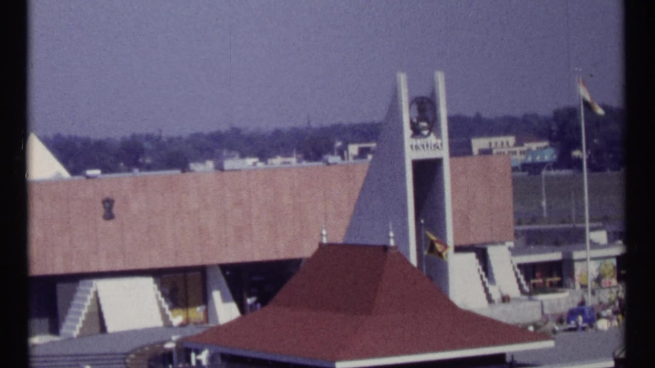 Modernist building with tall tower, India sign, flags, and red roof canopy.