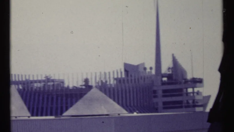 1967 Montreal frame showing modernist architectural forms, a tall spire, ribbed wall elements, and pale sky.