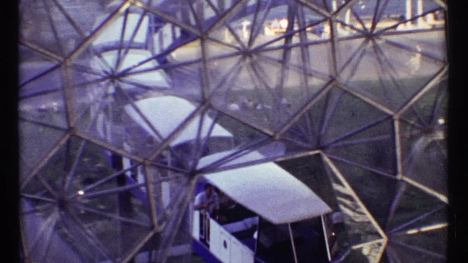A small train with visible passengers moves through the lower area of the 1967 Montreal geodesic structure.