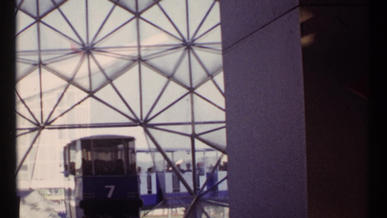 Tram car 7 approaches a station behind a triangular glass-and-metal wall.
