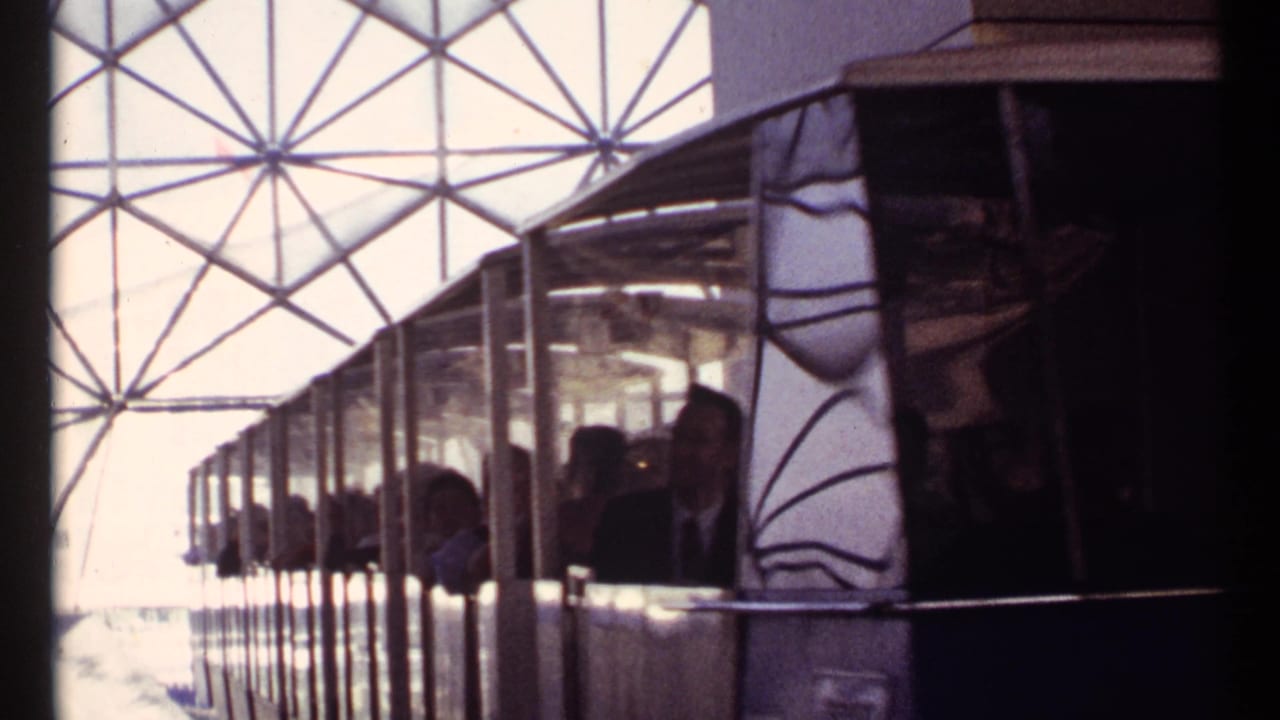 Train car with passengers passing under a geodesic roof structure.