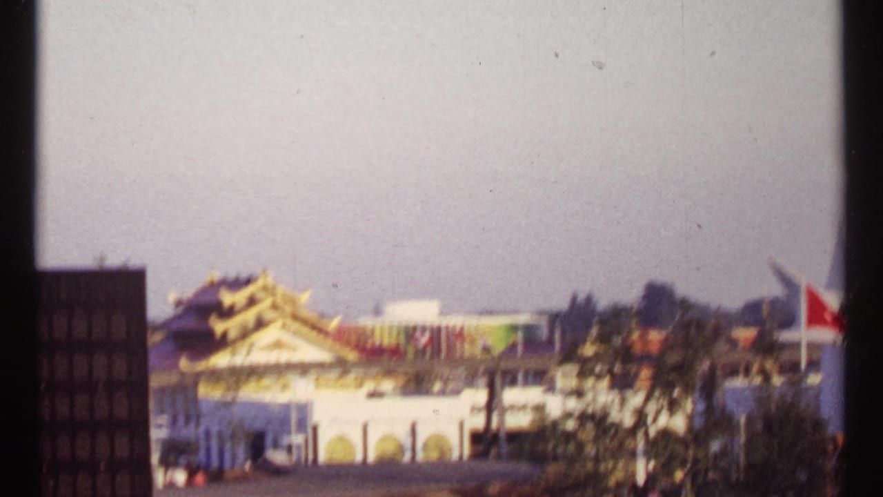 Montreal Expo 67 fairground view with Asian-style rooflines, flags, and exhibition buildings in soft 8mm focus.