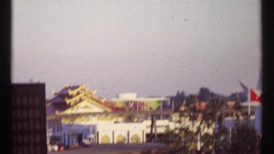 Montreal Expo 67 fairground view with Asian-style rooflines, flags, and exhibition buildings in soft 8mm focus.